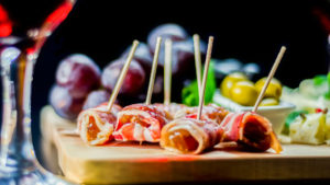 Delicious appetizer of figs wrapped in bacon served with blue cheese, grapes and olives, catering set for the party